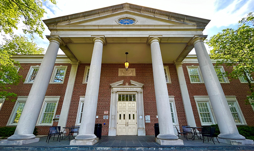 Shot of an imposing brick library building with four large white columns and a party cloudy sky above,