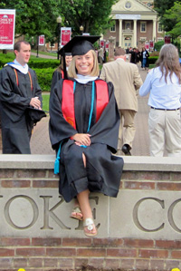 graduate with stoles and cords sitting on the roanoke college sign