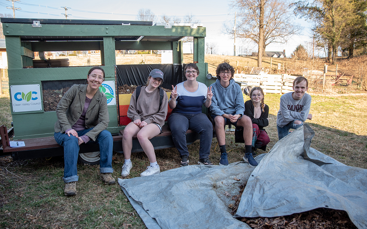 A professor and five students sit on the edge of a trailer they've filled with compostable material for a class project.