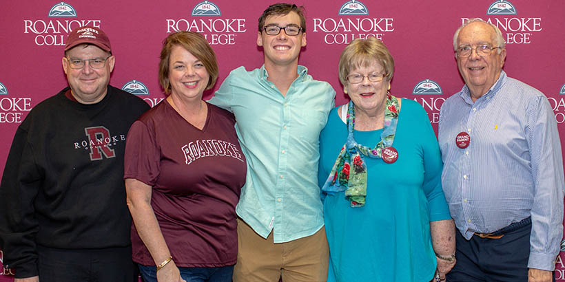 A family posing for a photo in front of the Roanoke College backdrop