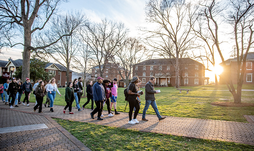 Students and faculty walk together across the Front Quad as the setting sun glints in the background