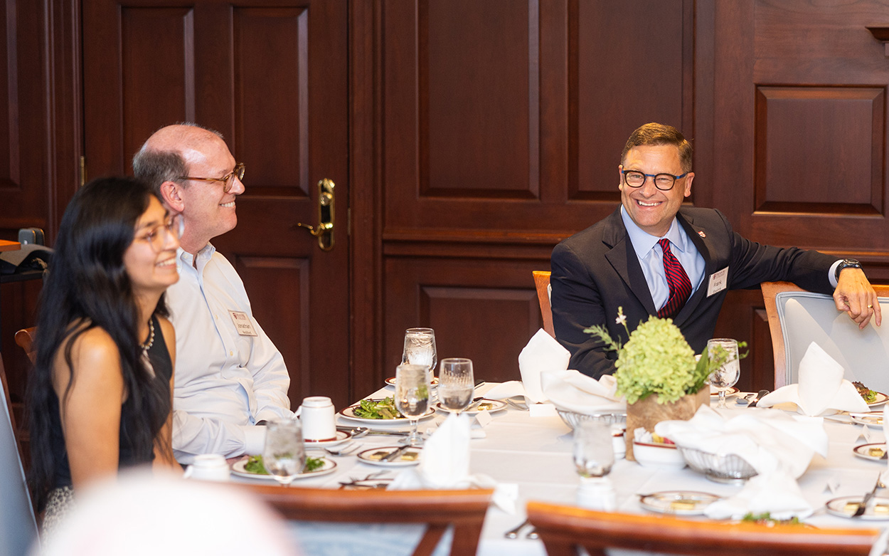 Jonathan Reckford, President Shushok and a student laugh while seated together around a dinner table