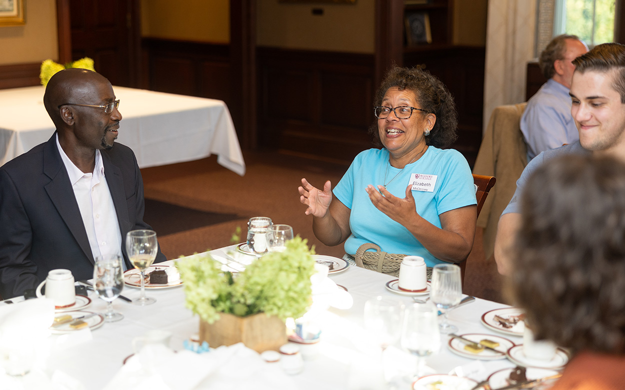 Faculty and campus leaders laugh while seated together at a dining table