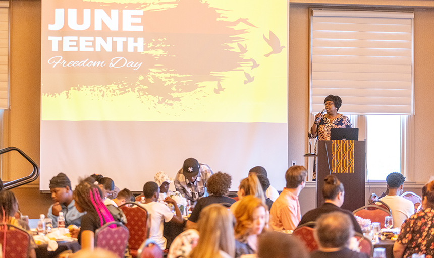 Vice President for Community, Diversity and Inclusion Teresa Ramey speaks at the campus celebration against a backdrop of an image that reads Juneteenth: Freedom Day
