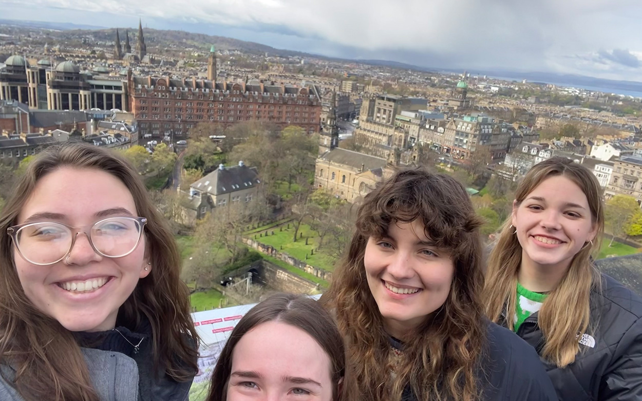 Becca Moorman and friends smiling for a photo with a sweeping city viewshed in the background