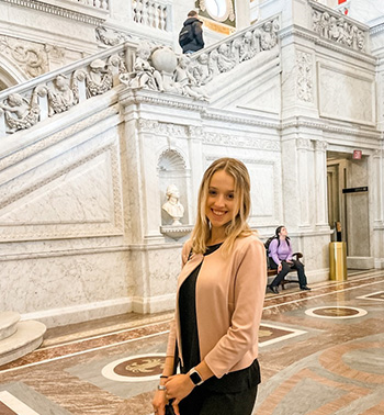 Megan Onofrei smiles next to an intricately carved, historical stairway in a D.C. building