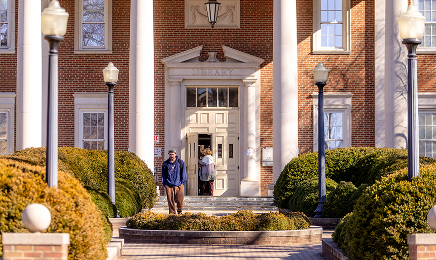 Students enter and leave through the front doors of a large red brick building with white columns.