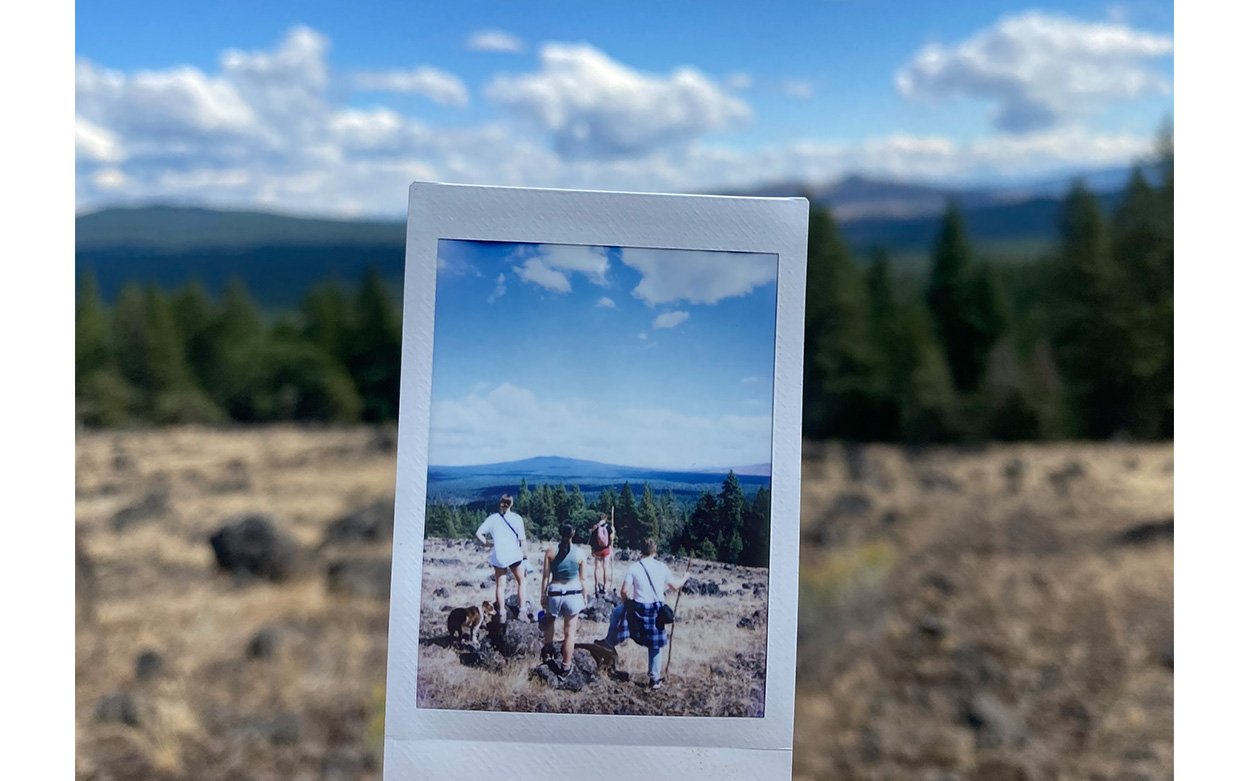 Polaroid photo of students hiking being held up against a backdrop of a mountain vista