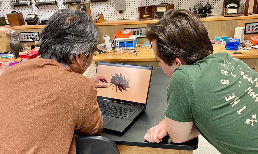 A professor and a student lean over a laptop with an image of a starshade pulled up on its screen