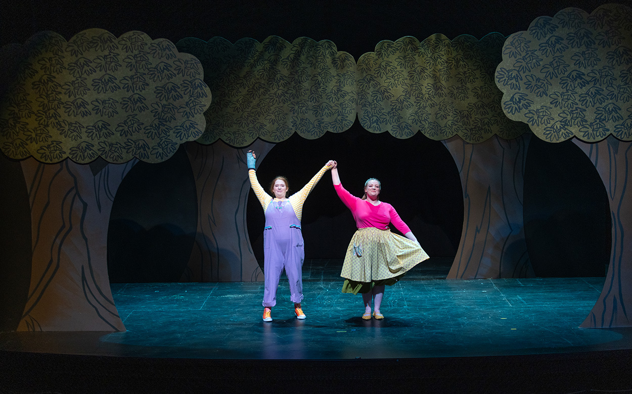 Two actresses hold their arms aloft in the air while taking their final bow on stage