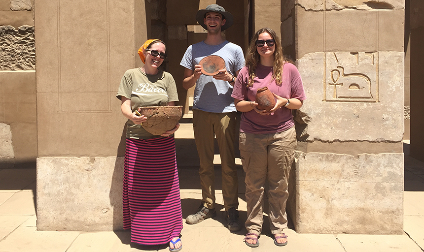 Dr. Leslie Warden and students Jacob Friedrich and Serena Soterakopoulos hold artifacts 