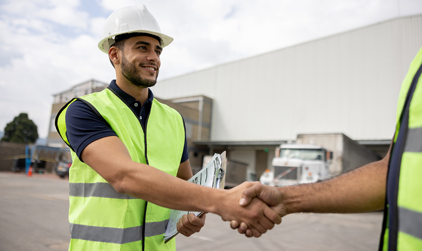 Man shaking hands with another person both wearing safety vests and hardhats