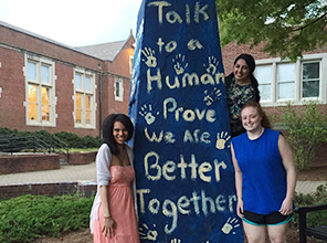 Students posing by the Monument where "talk to a human, prove we are better together" has been written