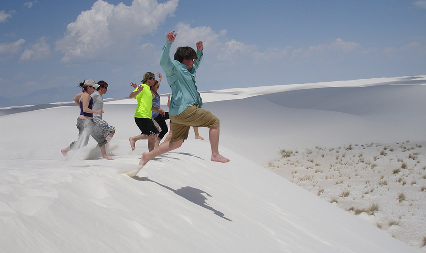 Students jumping in sand dunes