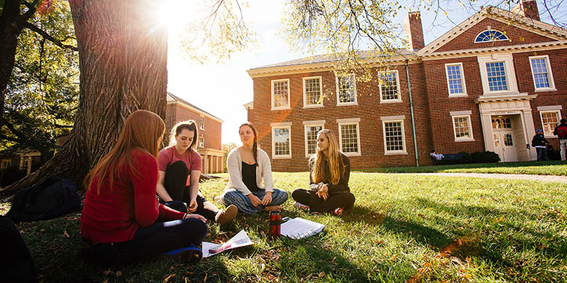 students sitting on the grass in front of lucas hall doing work