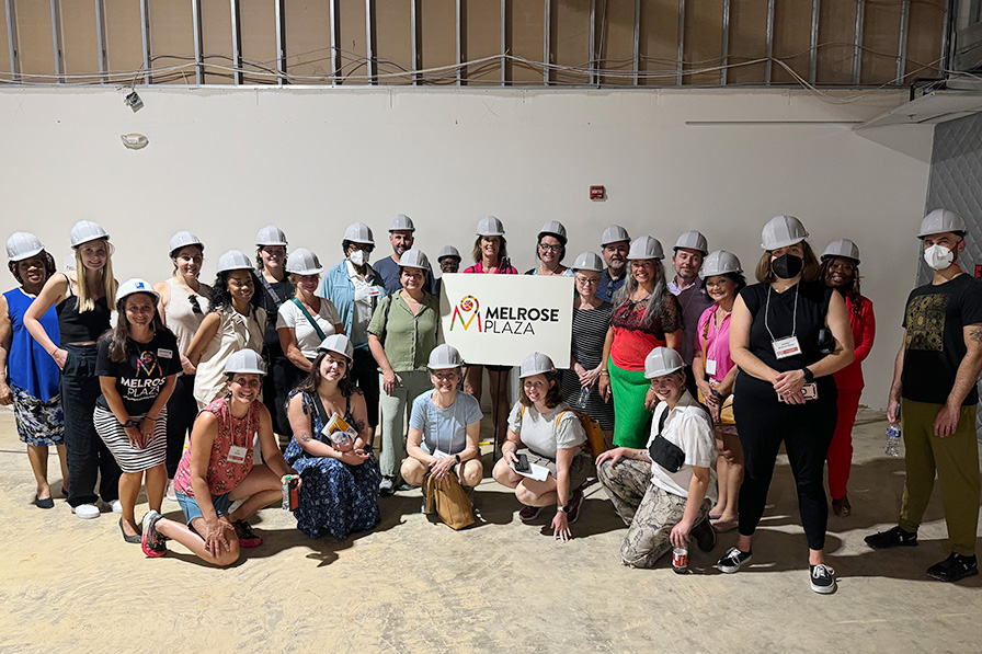 Group of community members wearing hard hats and holding a sign that says Melrose Plaza