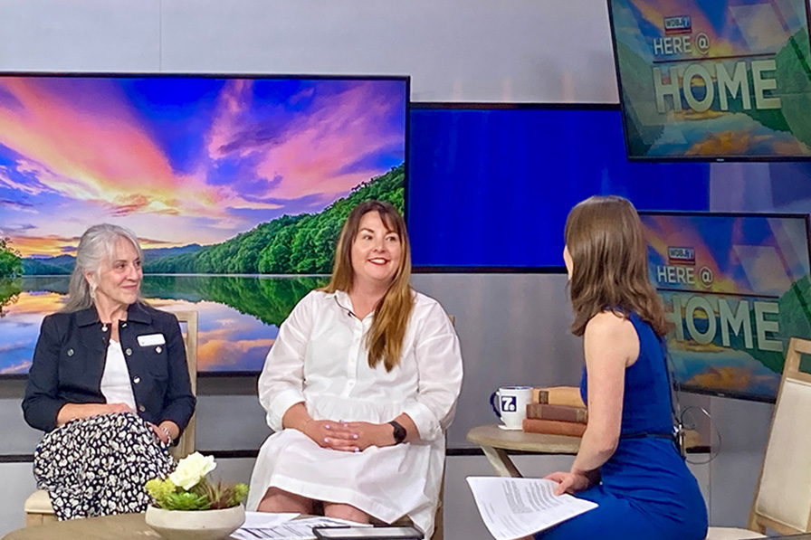 Two people smiling while being interviewed by a reporter on a TV set