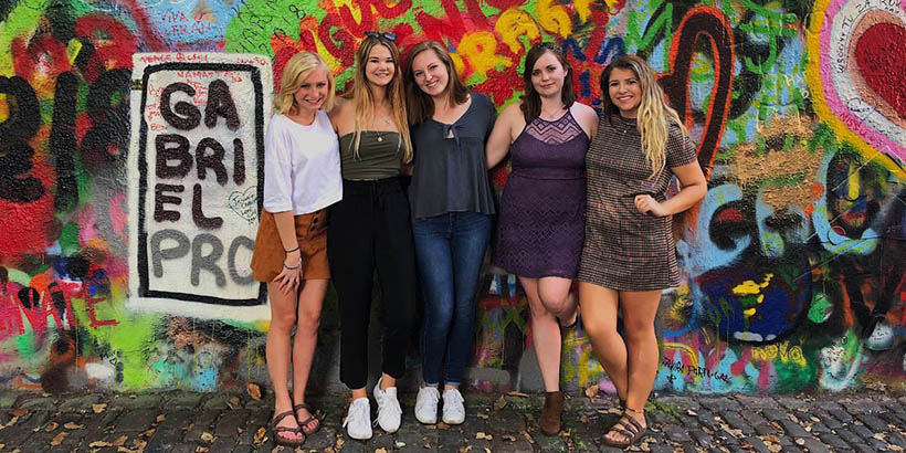 Students standing in front of a wall coated in graffiti