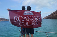 Two people standing on a boat holding Roanoke College flag