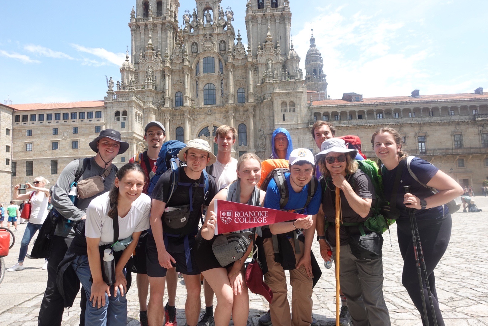 students smiling for a group photo with a roanoke college pennant flag during an immersive learning trip to europe