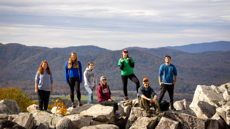 Students smiling for a photo on a hike with a mountain view in the background