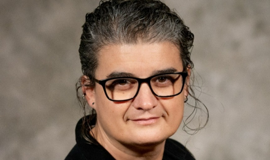 image of woman with black glasses, dark hair pulled back, and a black blouse, posing for the camera