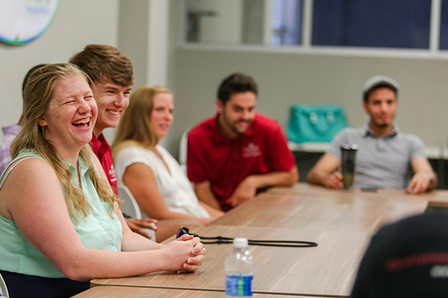 students seated at a table laugh during an event on campus