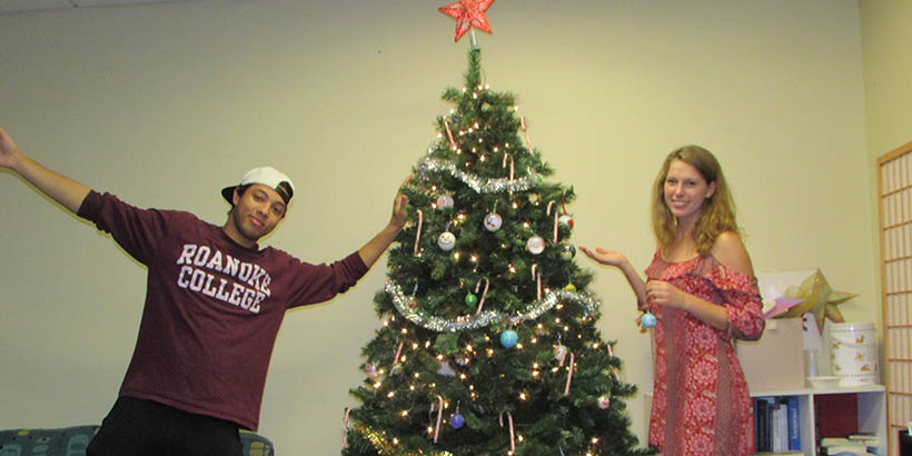 Two students posing for a photo by a Christmas tree