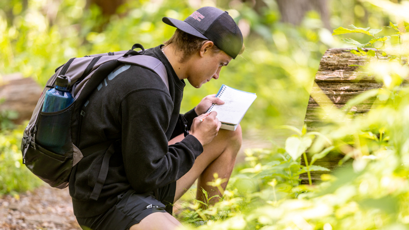 student outside writing in a notebook