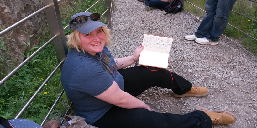 A student holds up their sketchbook to reveal their drawings