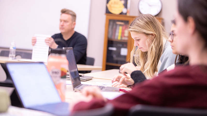 students in class with laptops with professor 