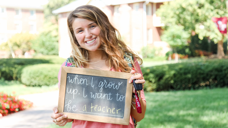 Students holding a chalkboard that says "when I grow up, I want to be a teacher"