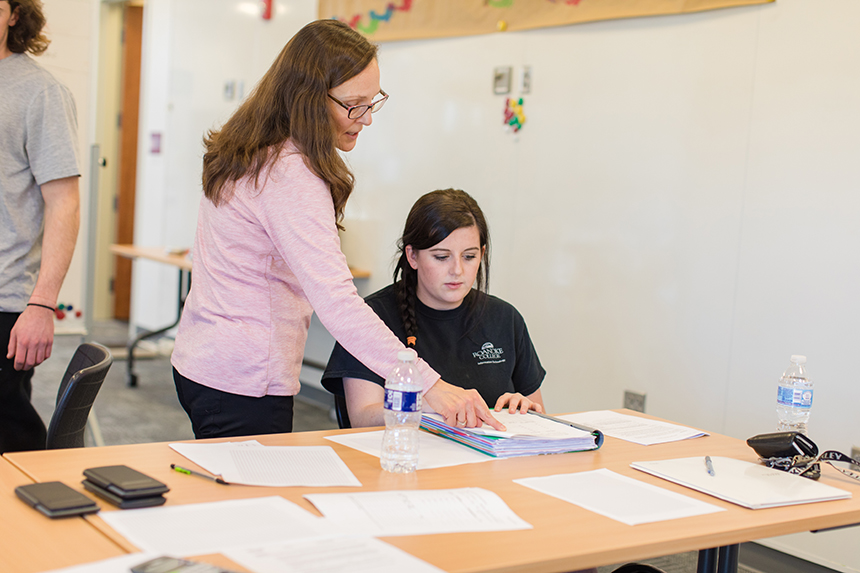 A professor talks with a student while they examine a book together