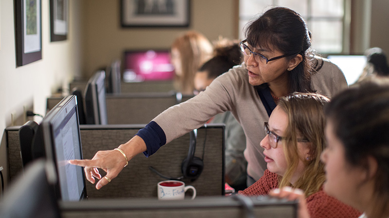 professor points at a student's computer screen while helping them during a class