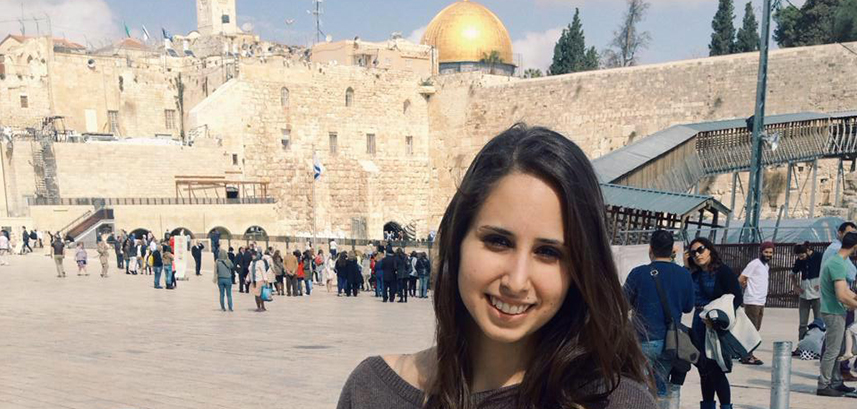 A woman stands in front  of historic buildings 