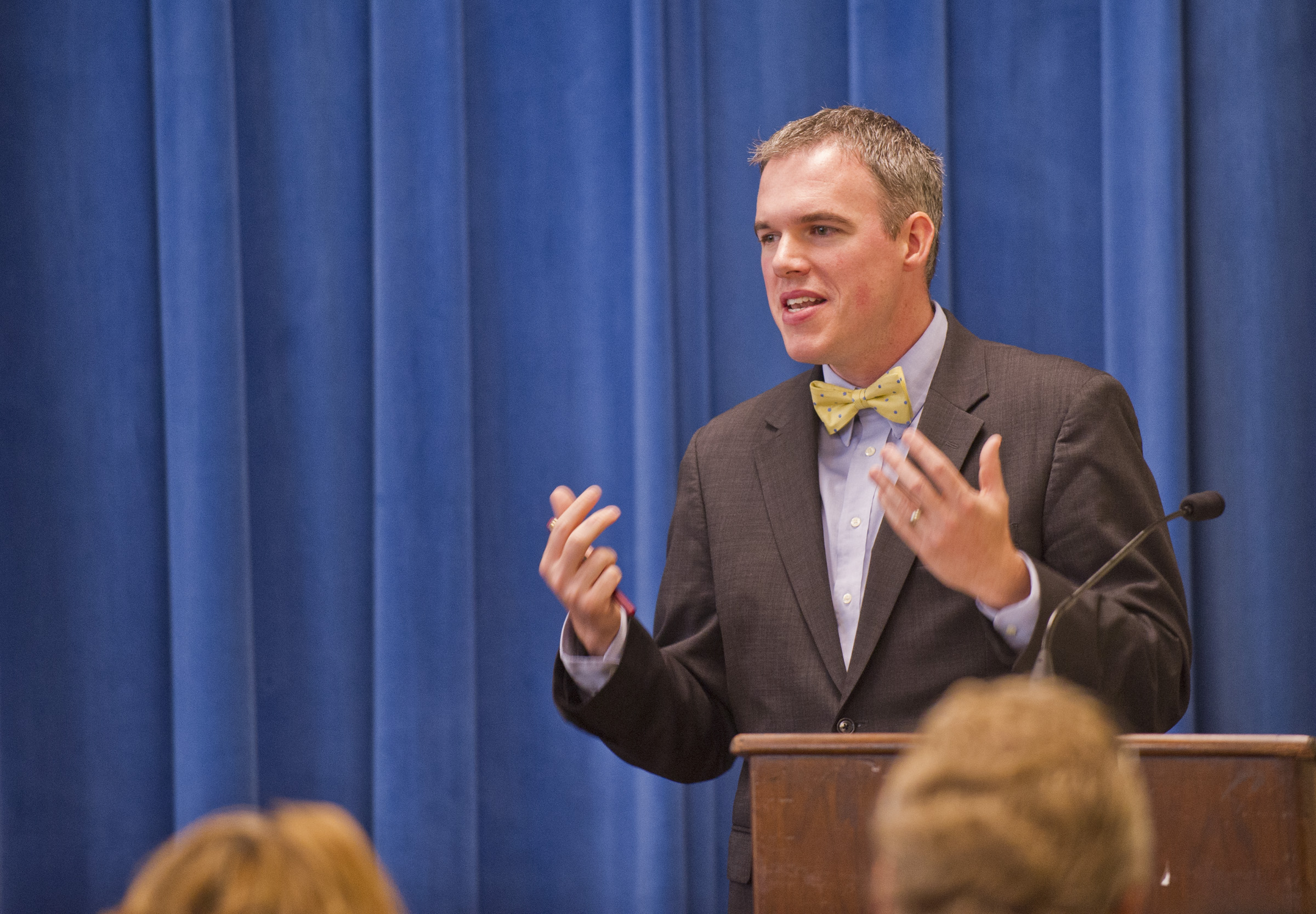 man stands at a podium with stage curtain behind him