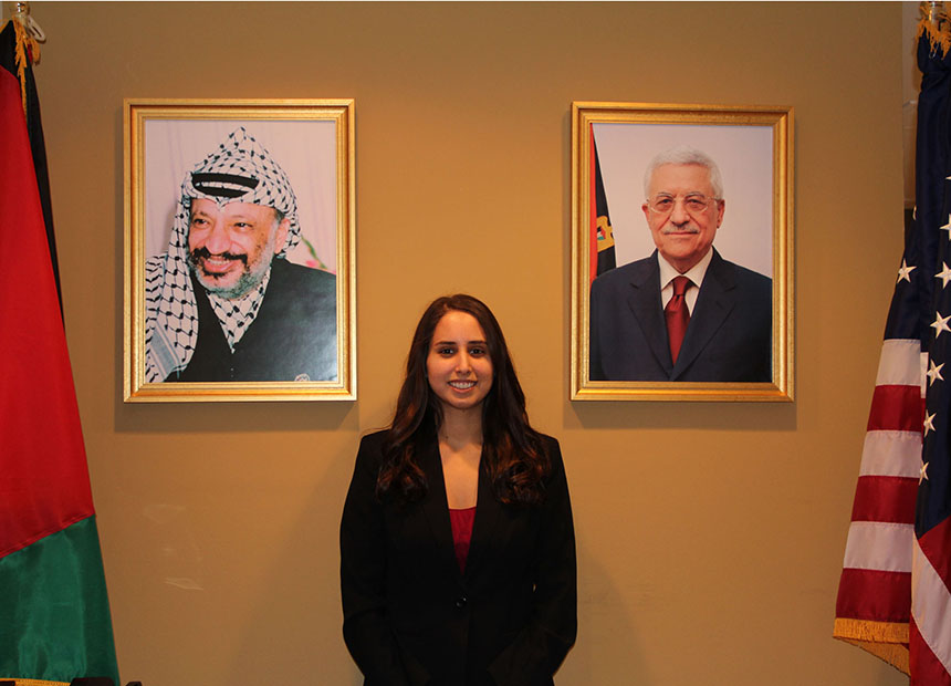 Student posing by portraits in a government building