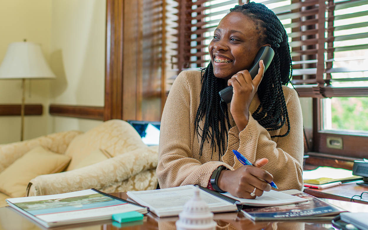 Olivia Kitt '20 holding a phone to her ear and writing notes in a notebook.