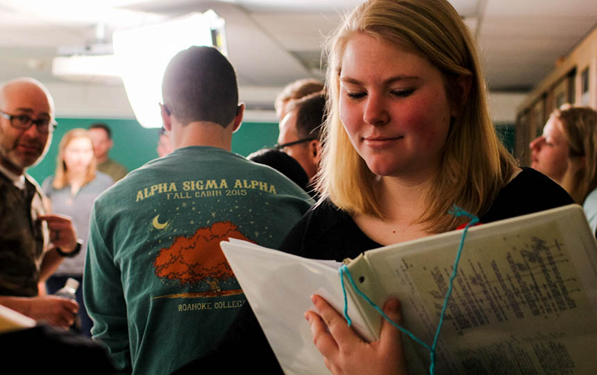 Student looking in notebook with several people standing behind her