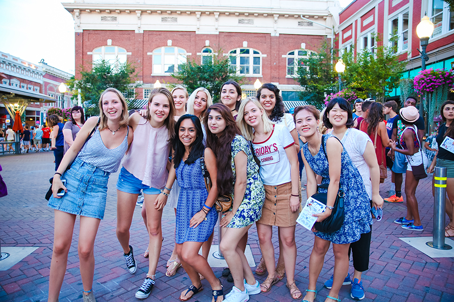 A group of young women pose for a photo in Market Square in downtown Roaonke. Brick buildings are in the background.
