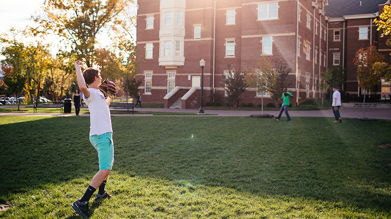 student in front of a residence hall throwing the football