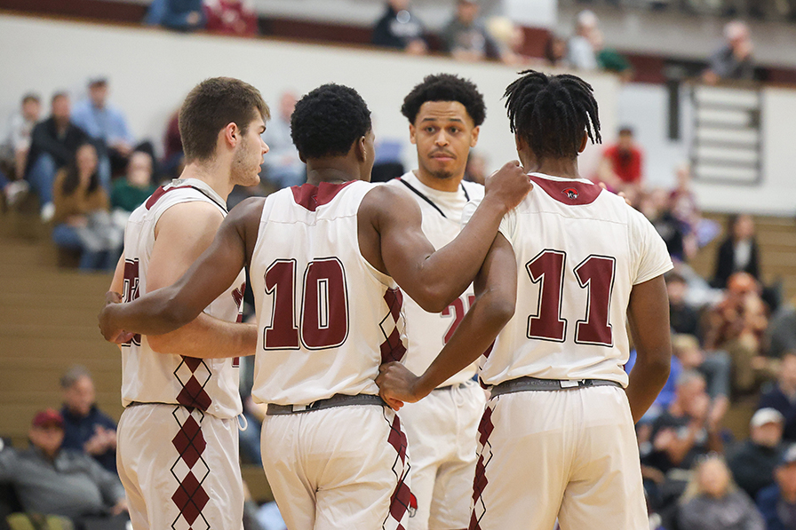 Four basketball players in Roanoke uniforms huddle on the court