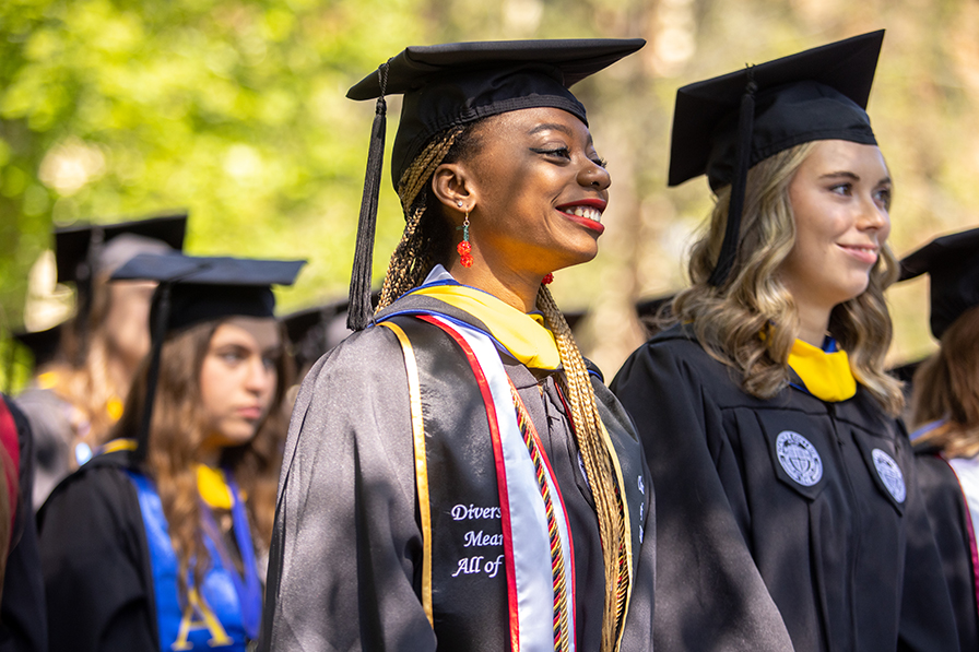 Two young women in black graduation robes and caps smile