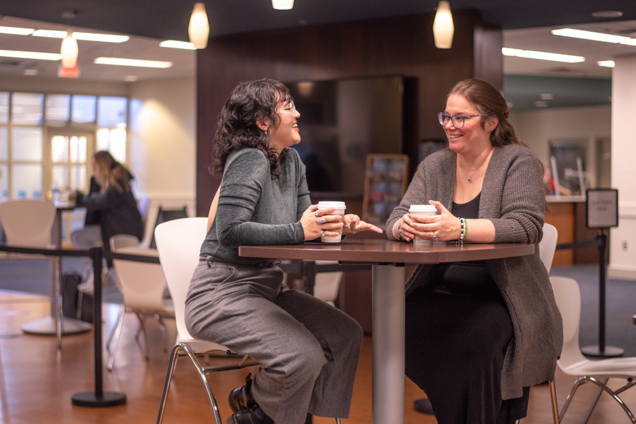 A professor and a student sit at a high-top table at Rooney's Brews, where they are involved in a conversation.