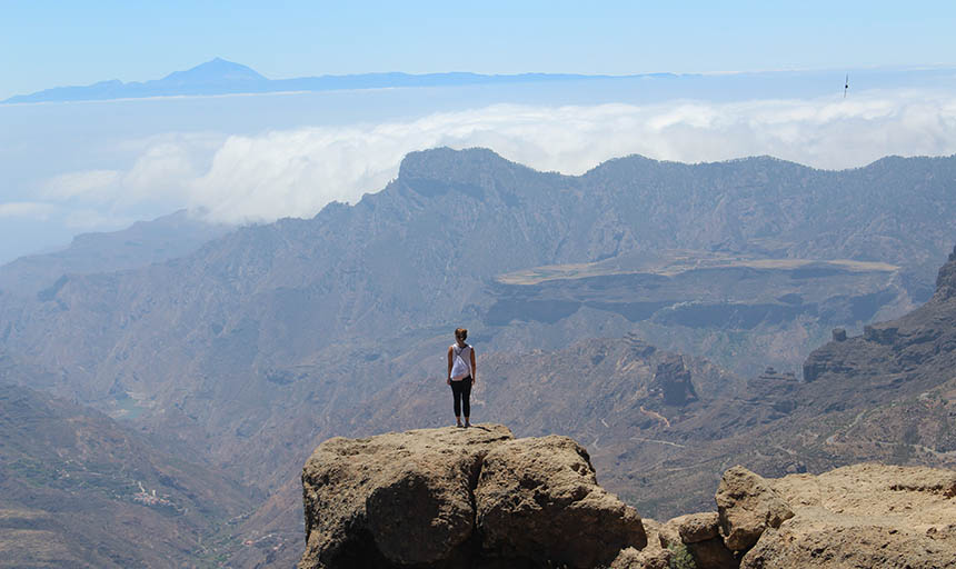 student standing on a rock on a cliff looking out at the view