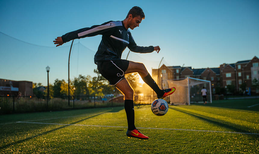 A member of the men's soccer team kicking a soccer ball into the air