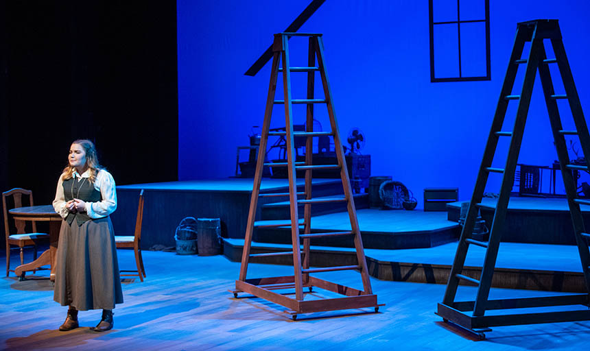 A student acting on a stage with ladders behind her