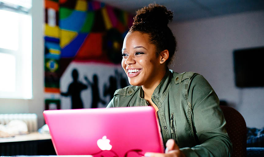 A student smiling and sitting at her laptop