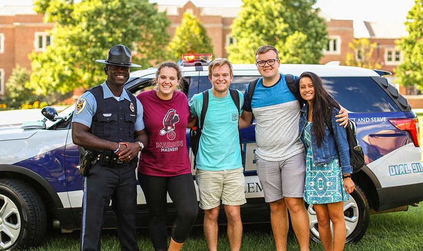 A photo of a salem police officer and four students. 2 of the students are women and 2 are men. They are standing in front of a police car
