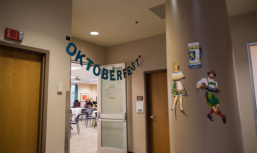 Sign saying "Oktoberfest" above a door. Two posters of people in dirndl and lederhosen on a post outside. 
